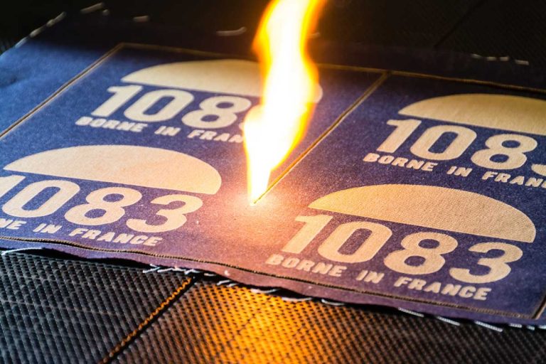 Close-up of a laser machine engraving letters and a logo onto denim textile, showcasing precision and detail.